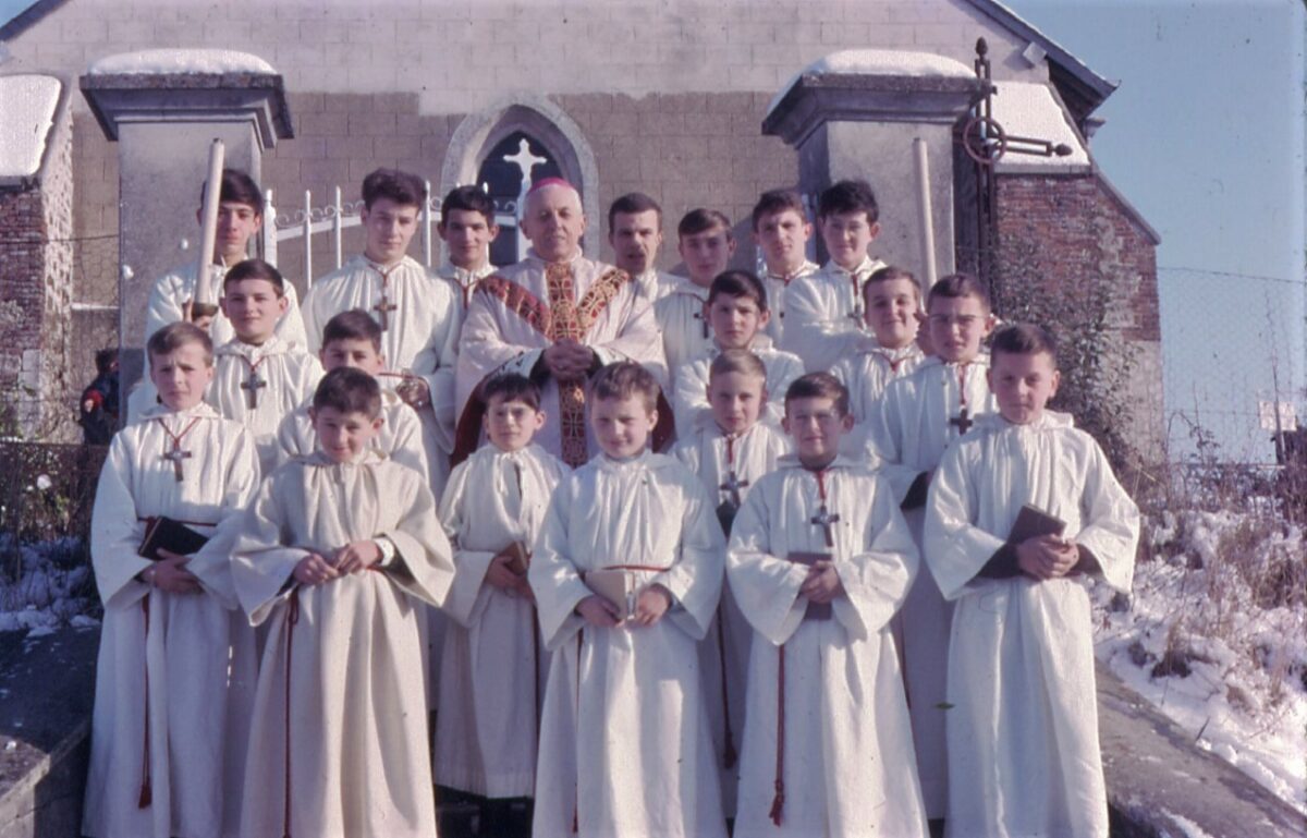 Monseigneur François Marty et enfants de chœur devant la grille de l'église Saint-Jean à La Romagne (Ardennes).