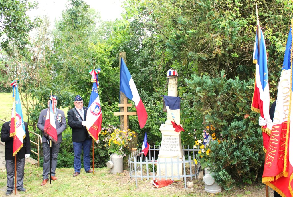 Trois porte-drapeau de Union nationale des combattants de Chaumont-Porcien (Ardennes), monsieur Michel Mauroy de La Romagne (Ardennes) avec son clairon, stèle des fusillés de Wadimont (Ardennes) avec un drapeau du comité de Chaumont-Porcien (Ardennes) du Souvenir français, une croix de Lorraine et d'autres symboles de la Résistance française. Prise de vue effectuée le vendredi 30 août 2024 à Wadimont (Ardennes). Crédits photographiques : © 2020 laromagne.info par Marie-Noëlle ESTIEZ BONHOMME.