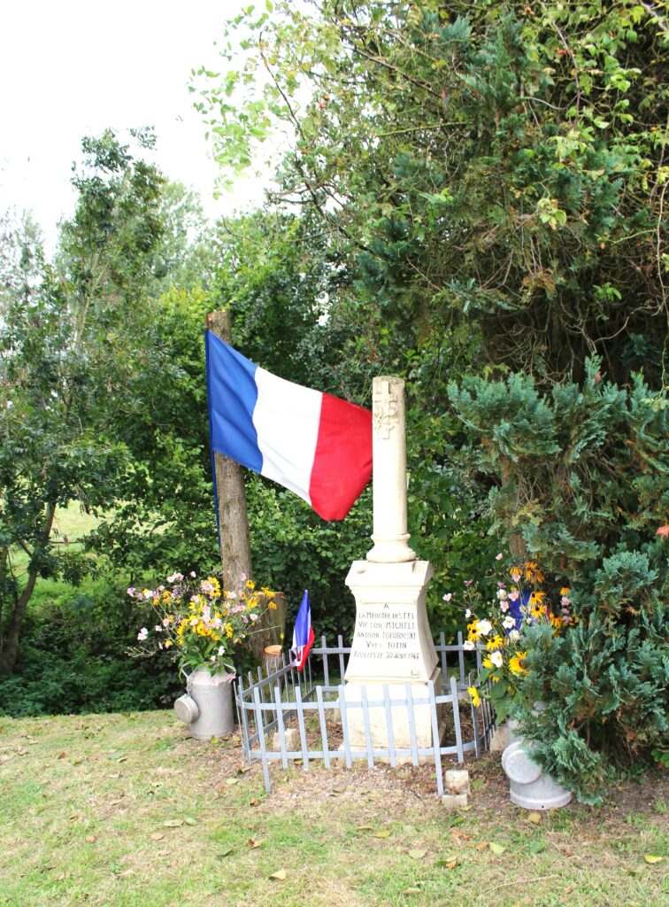 Stèle des fusillés, lors de la cérémonie du quatre-vingtième anniversaire. En matière de symbolique funéraire, la colonne brisée (ou tronquée) est un élément funéraire choisi pour honorer des personnes décédées prématurément et dans la force de l’âge. Prise de vue effectuée le vendredi 30 août 2024 à Wadimont (Ardennes). Crédits photographiques : © 2020 laromagne.info par Marie-Noëlle ESTIEZ BONHOMME.