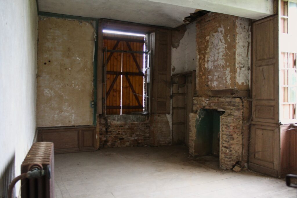 Les cheminées des chambres du premier étage ont été démolies, tandis que certaines taques de cheminée subsistent encore dans le château de Rocquigny (Ardennes). Celle de la salle à manger du rez-de-chaussée est ornée d’un tournesol et d’une couronne perlée, tandis que la grande salle du deuxième étage possède une taque fleurdelysée. Ces éléments décoratifs témoignent du soin apporté aux détails ornementaux. Photographies en couleurs, prises de vue effectuées le vendredi 18 octobre 2024. Crédits photographiques : © 2020 laromagne.info par Marie-Noëlle ESTIEZ BONHOMME.