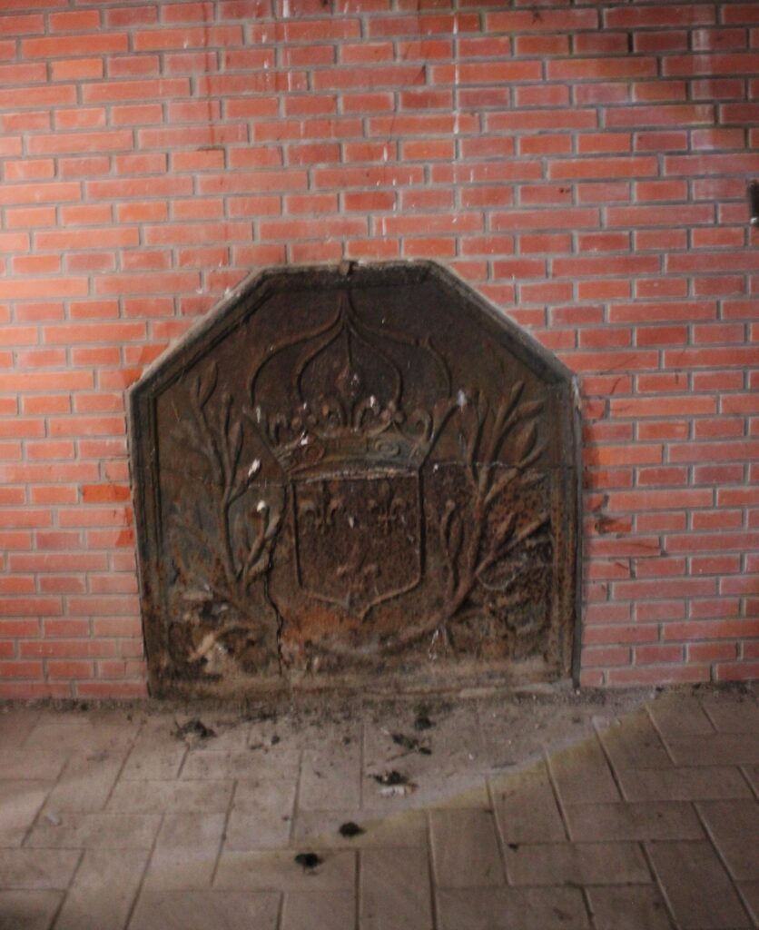 Les cheminées des chambres du premier étage ont été démolies, tandis que certaines taques de cheminée subsistent encore dans le château de Rocquigny (Ardennes). Celle de la salle à manger du rez-de-chaussée est ornée d’un tournesol et d’une couronne perlée, tandis que la grande salle du deuxième étage possède une taque fleurdelysée. Ces éléments décoratifs témoignent du soin apporté aux détails ornementaux. Photographies en couleurs, prises de vue effectuées le vendredi 18 octobre 2024. Crédits photographiques : © 2020 laromagne.info par Marie-Noëlle ESTIEZ BONHOMME.