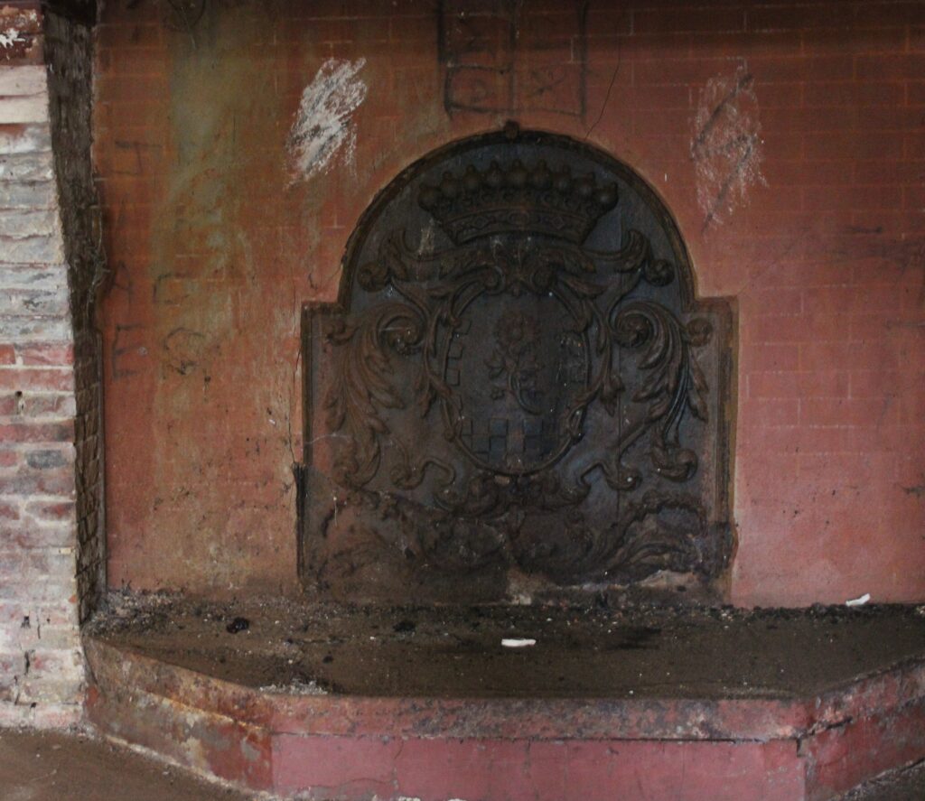 Les cheminées des chambres du premier étage ont été démolies, tandis que certaines taques de cheminée subsistent encore dans le château de Rocquigny (Ardennes). Celle de la salle à manger du rez-de-chaussée est ornée d’un tournesol et d’une couronne perlée, tandis que la grande salle du deuxième étage possède une taque fleurdelysée. Ces éléments décoratifs témoignent du soin apporté aux détails ornementaux. Photographies en couleurs, prises de vue effectuées le vendredi 18 octobre 2024. Crédits photographiques : © 2020 laromagne.info par Marie-Noëlle ESTIEZ BONHOMME.