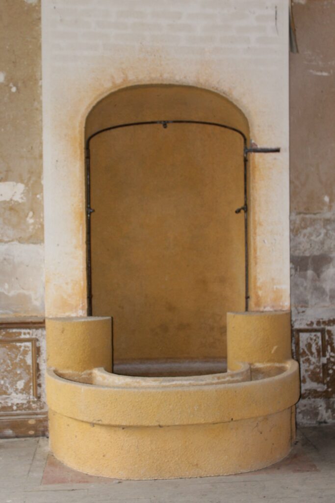 Dans le salon, au rez-de-chaussée du château de Rocquigny (Ardennes), à gauche de l'entrée, se trouve une fontaine décorative et commémorative dédiée à Jean Mermoz. Cette fontaine rend hommage à l'aviateur français et figure emblématique de l'Aéropostale. Placée dans cet espace de réception, elle incarne un souvenir marquant. Photographie en couleurs, prise de vue effectuée le vendredi 18 octobre 2024. Crédits photographiques : © 2020 laromagne.info par Marie-Noëlle ESTIEZ BONHOMME.