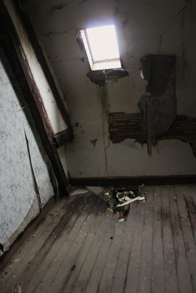 Des infiltrations d’eau de pluie affectent la grande pièce du deuxième étage du château de Rocquigny (Ardennes), autrefois aménagée en dortoir. L’humidité progressive a fragilisé les revêtements et laissé des traces visibles sur les murs et le plafond, témoignant de l’altération du bâti au fil du temps. Crédits photographiques : © 2020 laromagne.info par Marie-Noëlle ESTIEZ BONHOMME.