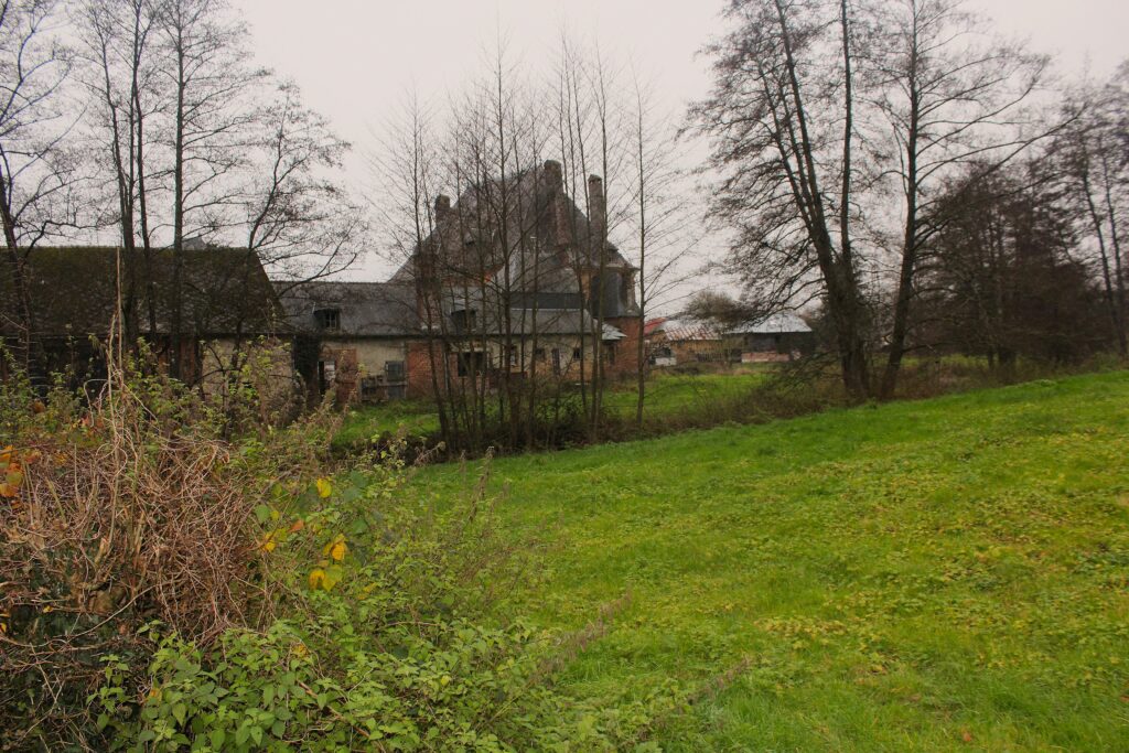 Façade nord du château de Rocquigny (Ardennes), avec une vue qui s’ouvre sur les communs partiellement dissimulée derrière un rideau d’arbres. Photographies en couleurs, prises de vue effectuées le jeudi 12 décembre 2024. Crédits photographiques : © 2020 laromagne.info par Marie-Noëlle ESTIEZ BONHOMME.