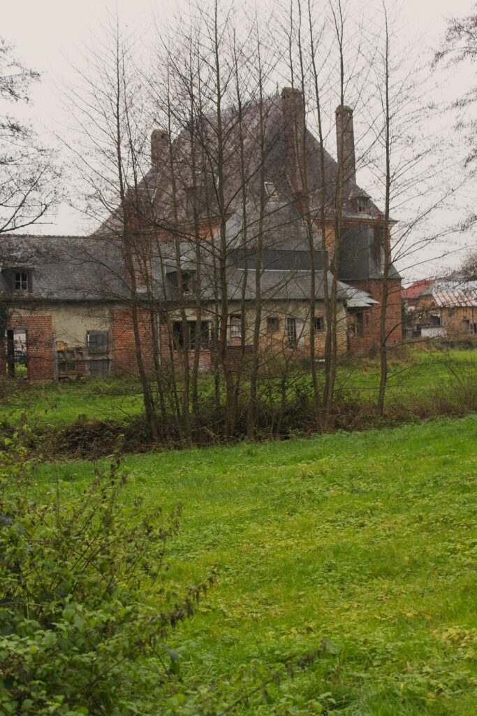 Façade nord du château de Rocquigny (Ardennes), avec une vue qui s’ouvre sur les communs partiellement dissimulée derrière un rideau d’arbres. Photographies en couleurs, prises de vue effectuées le jeudi 12 décembre 2024. Crédits photographiques : © 2020 laromagne.info par Marie-Noëlle ESTIEZ BONHOMME.