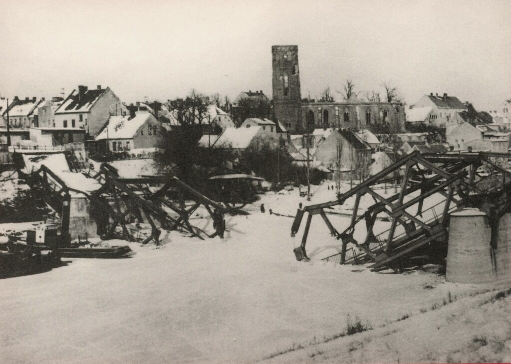 „Gesprengte Neue Deichbrücke (I). Von 1945 bis 1996 ersetzte die Fähre die gesprengte Deichbrücke.“
Reproduction moderne d'une carte postale ancienne issue du lot Historische Brückeansichten von Fürstenberg/Oder (Vues historiques du pont de Fürstenberg/Oder). Collection personnelle de l'auteure.