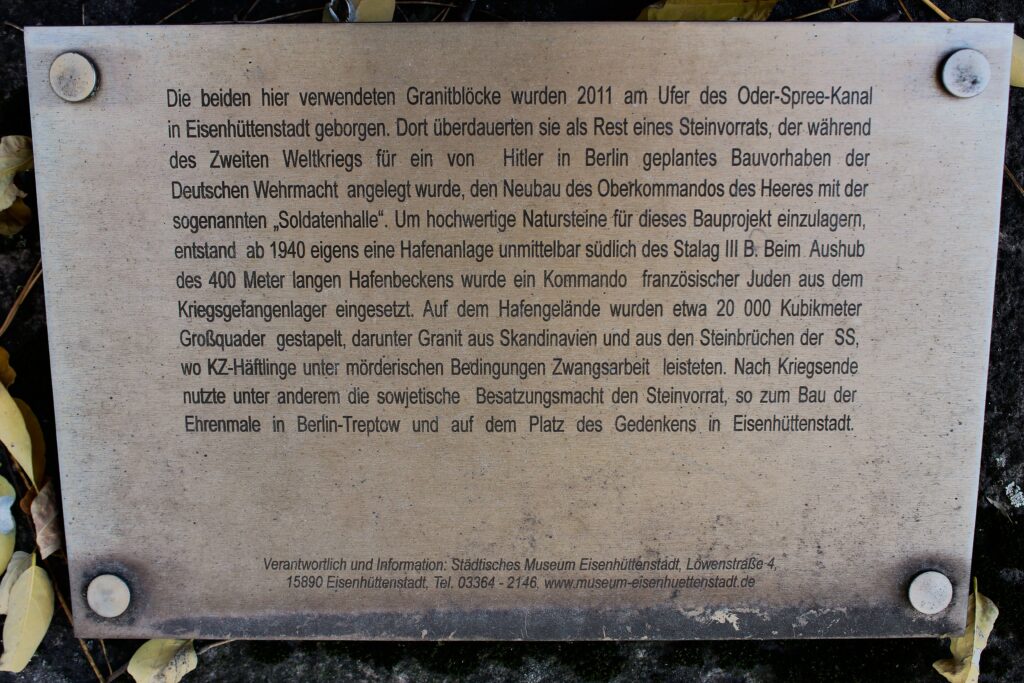 « Les deux blocs de granit utilisés ici ont été récupérés en 2011 sur les rives du canal Oder-Spree à Eisenhüttenstadt. Ils y avaient survécu comme vestiges d'un stock de pierres constitué pendant la Seconde Guerre mondiale pour un projet de construction de la Wehrmacht prévu par Hitler à Berlin, à savoir le nouveau quartier général de l'armée avec la 'halle des soldats'. Afin de stocker des pierres naturelles de haute qualité pour ce projet de construction, une installation portuaire a été spécialement construite à partir de 1940, juste au sud du Stalag III-B. Un commando de juifs français du camp de prisonniers de guerre a été utilisé pour creuser le bassin portuaire de 400 mètres de long. Environ 20 000 mètres cubes de gros blocs de pierre ont été empilés sur le site portuaire, dont du granit provenant de Scandinavie et des carrières de la SS, où les détenus des camps de concentration étaient soumis à un travail forcé dans des conditions inhumaines. Après la fin de la guerre, les forces d'occupation soviétiques ont notamment utilisé ces réserves de pierres pour construire le mémorial de Berlin-Treptow et la place du Souvenir à Eisenhüttenstadt. »
Photographie en couleurs, prise de vue effectuée le vendredi 25 octobre 2024. Crédits photographiques : © 2020 laromagne.info par Marie-Noëlle ESTIEZ BONHOMME.