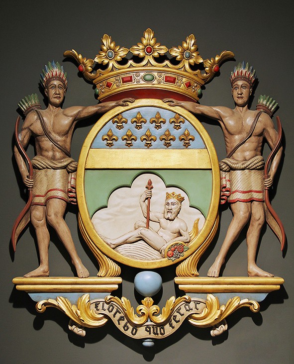 Musée de la Compagnie des Indes, Port-Louis (Morbihan). Blason de la Compagnie française des Indes : écu d’argent au chef d’azur semé de fleurs de lys d’or ; dans la partie inférieure, un fleuve couché au naturel s’appuie sur une corne d’abondance d’or. L’ensemble est timbré d’une couronne royale tréflée et soutenu par deux figures de « sauvages ». Devise : Florebo quocumqum ferar (« Je fleurirai partout où je serai portée »).