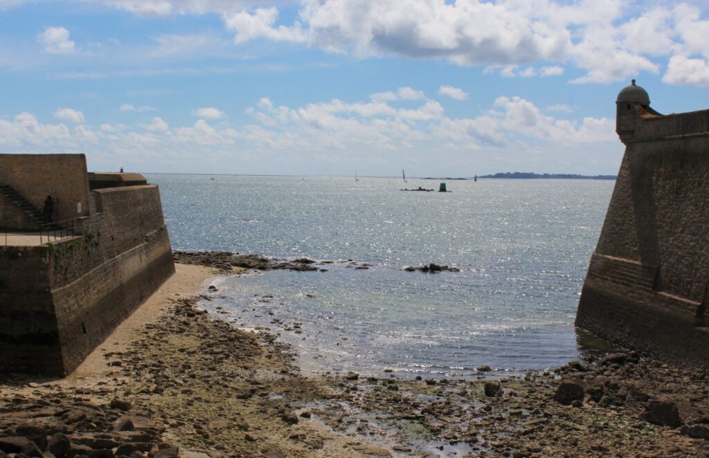 Depuis la citadelle de Port-Louis (Morbihan), le panorama s’ouvre sur la rade de Lorient, d’où partaient autrefois plusieurs navires de la Compagnie des Indes. Ce point stratégique permettait de surveiller les mouvements maritimes et de protéger le port d’attache. Photographie en couleurs, prise de vue effectuée le jeudi 17 avril 2025. Crédits photographiques : © 2020 laromagne.info par Marie-Noëlle ESTIEZ BONHOMME.
