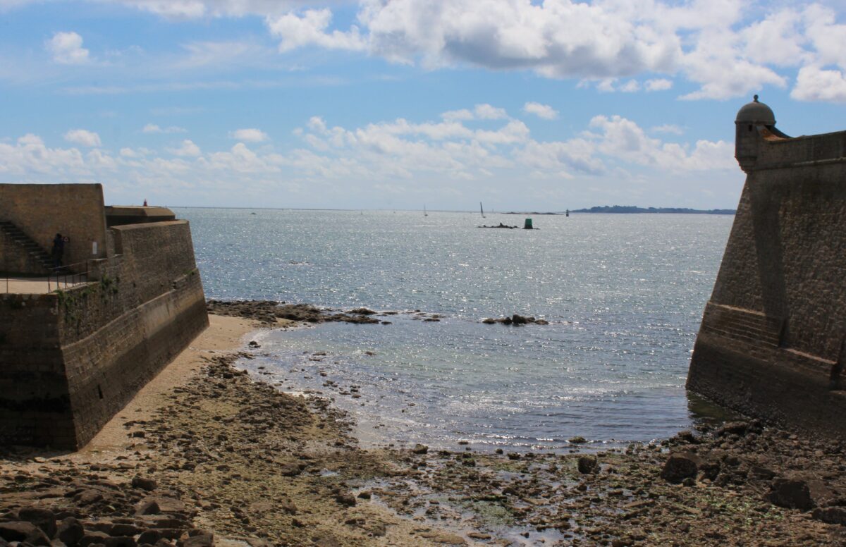 Depuis la citadelle de Port-Louis (Morbihan), le panorama s’ouvre sur la rade de Lorient, d’où partaient autrefois plusieurs navires de la Compagnie des Indes. Ce point stratégique permettait de surveiller les mouvements maritimes et de protéger le port d’attache. Photographie en couleurs, prise de vue effectuée le jeudi 17 avril 2025. Crédits photographiques : © 2020 laromagne.info par Marie-Noëlle ESTIEZ BONHOMME.