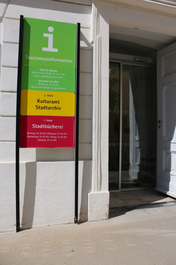 Signalétique de l’office de tourisme, des archives municipales et de la bibliothèque de Krems. Photographie en couleurs, prise de vue effectuée le mardi 1er juillet 2025. Crédits photographiques : © 2020 laromagne.info par Marie-Noëlle ESTIEZ BONHOMME.