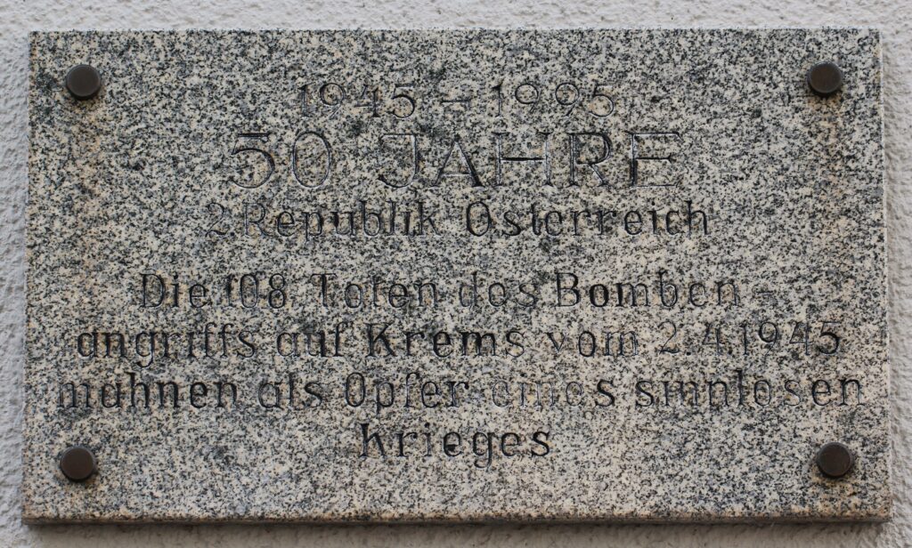 Plaque commémorative du bombardement de Krems, apposée à un mur de la gare. Photographie en couleurs, prise de vue effectuée le jeudi 3 juillet 2025. Crédits photographiques : © 2020 laromagne.info par Marie-Noëlle ESTIEZ BONHOMME.