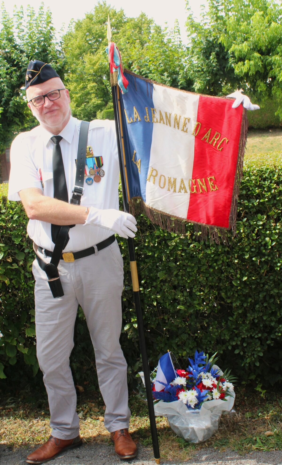 Confié à Didier Salamon, le drapeau brodé « Jeanne d'Arc » de La Romagne (Ardennes) a rappelé la richesse du patrimoine associatif et mémoriel de la commune. Photographie en couleurs, prise de vue réalisée le mardi 14 juillet 2026. Crédits photographiques : © 2020 laromagne.info par Marie-Noëlle ESTIEZ BONHOMME.