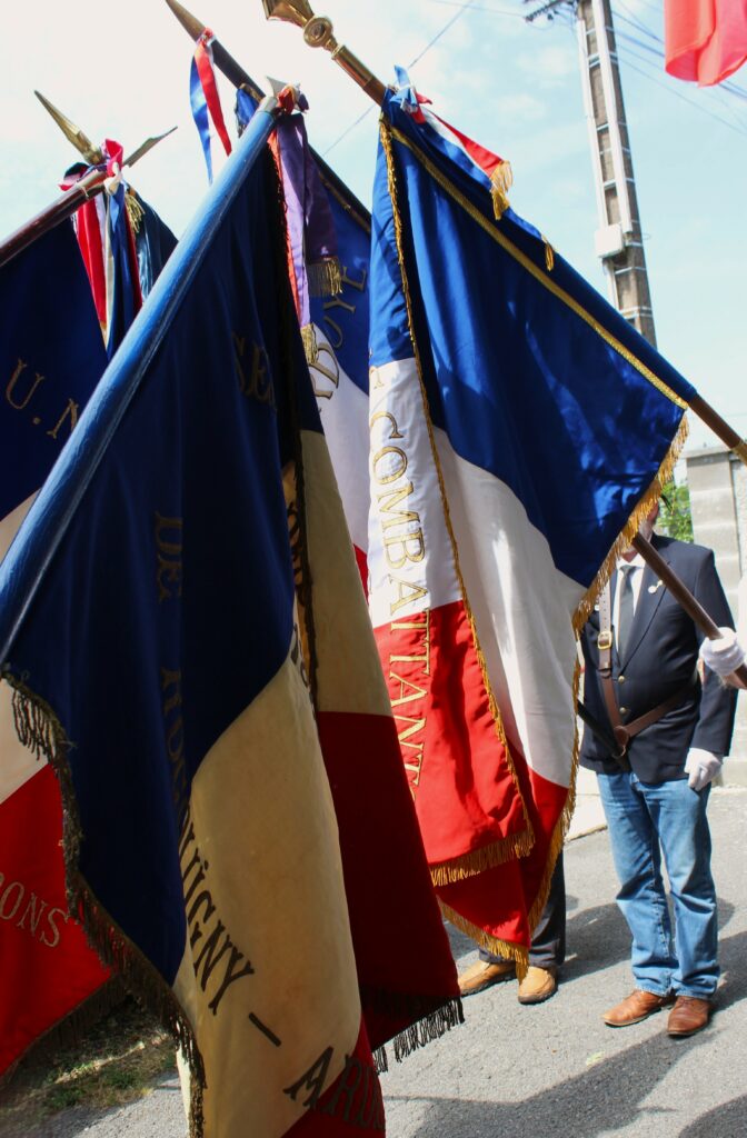 Les drapeaux sont inclinés durant a sonnerie aux morts et la minute de silence, puis redressés pour La Marseillaise. Photographie en couleurs, prise de vue réalisée le mardi 14 juillet 2026. Crédits photographiques : © 2020 laromagne.info par Marie-Noëlle ESTIEZ BONHOMME.
