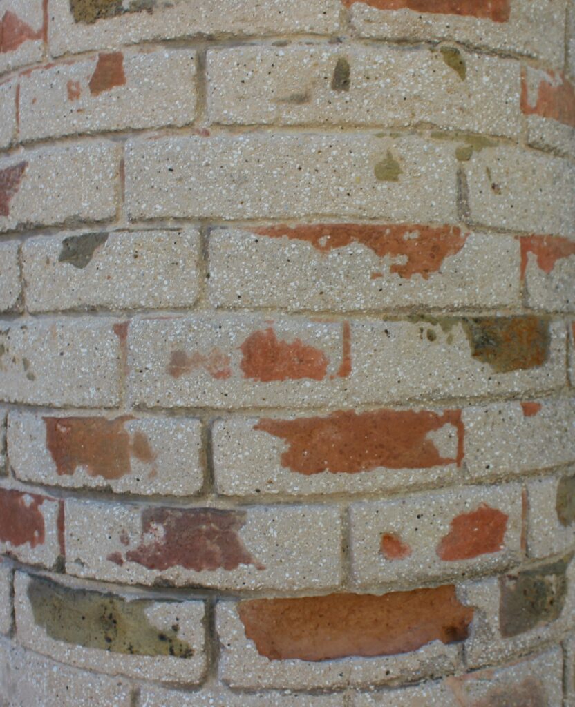 Ces briques des colonnes du porche d'accès de l'église Saint-Didier d'Asfeld (Ardennes) présentent une forme concave ou convexe, et ne comportent jamais de bords droits, ce qui constitue une particularité architecturale. Photographie en couleurs, prise de vue réalisée le samedi 25 avril 2026. Crédits photographiques : © 2020 laromagne.info par Marie-Noëlle ESTIEZ BONHOMME.